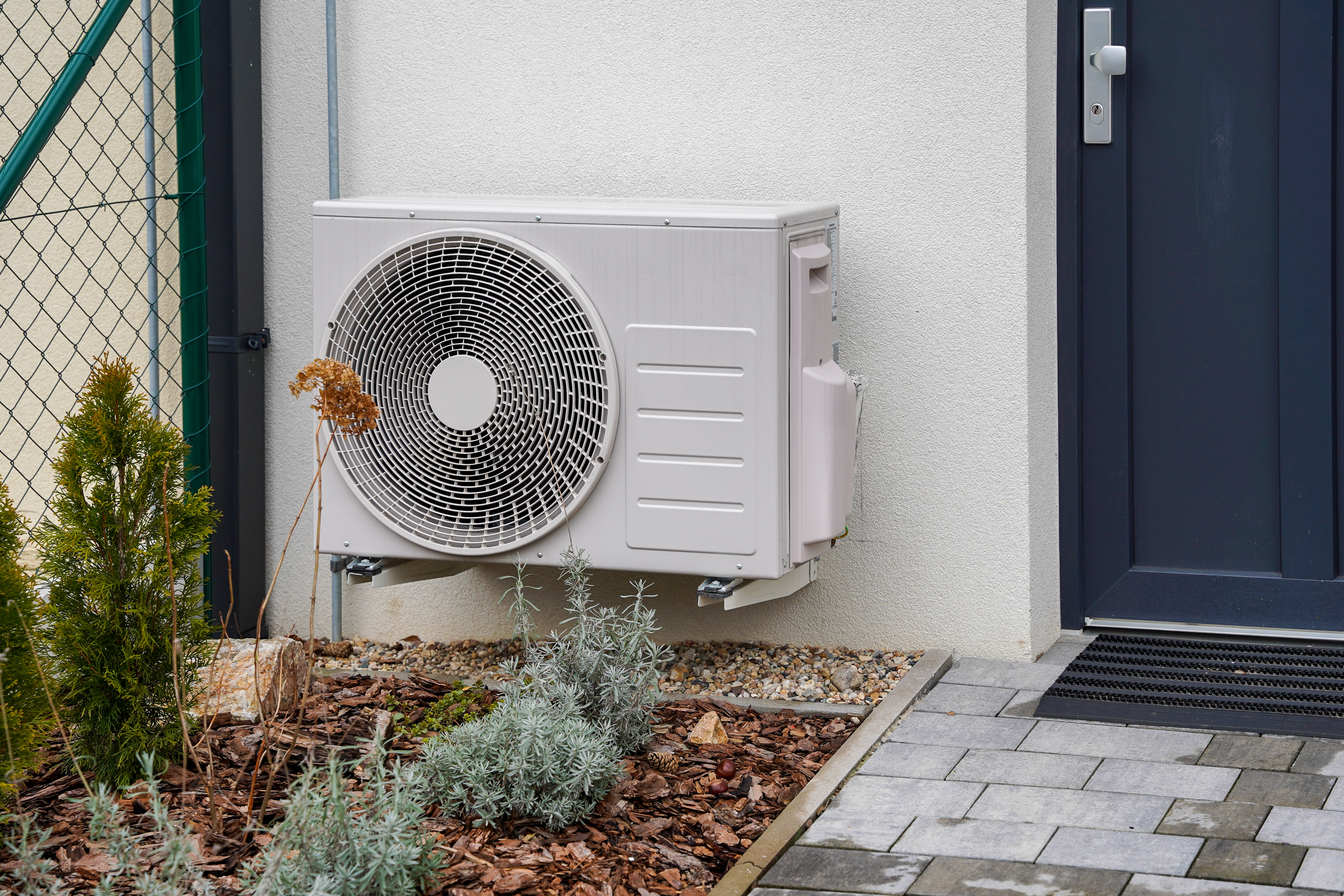 Air source heat pump beside front door of a house