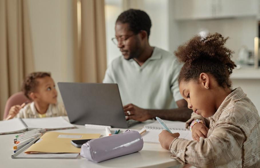 A man with his family at the dining table with a laptop