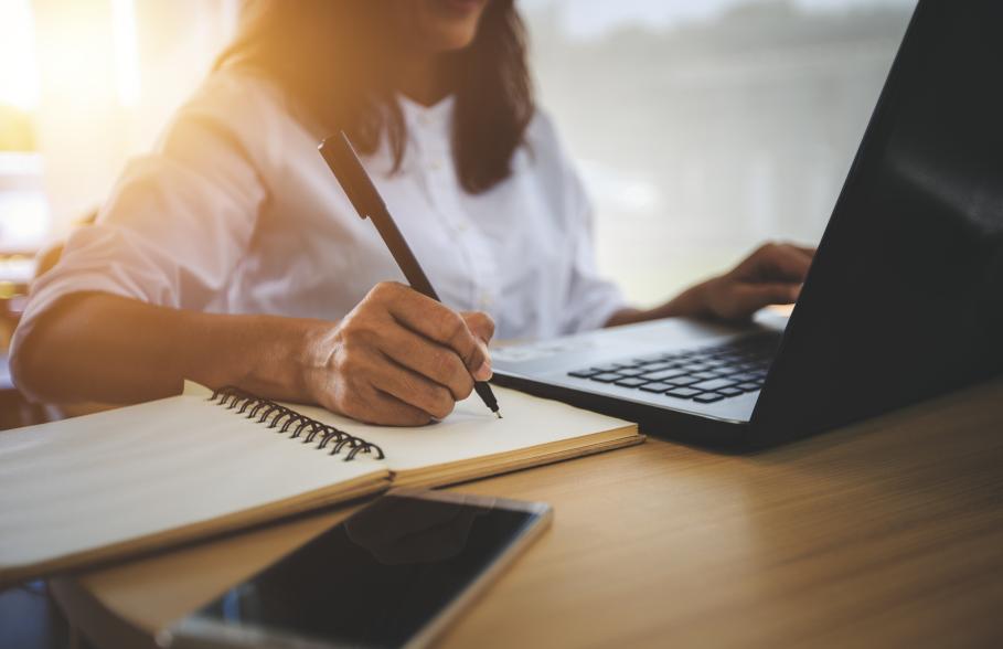 Person making notes in a book next to laptop