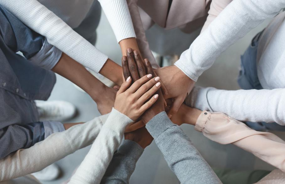 Seven people standing in a circle put their hands in and stack on top of each other