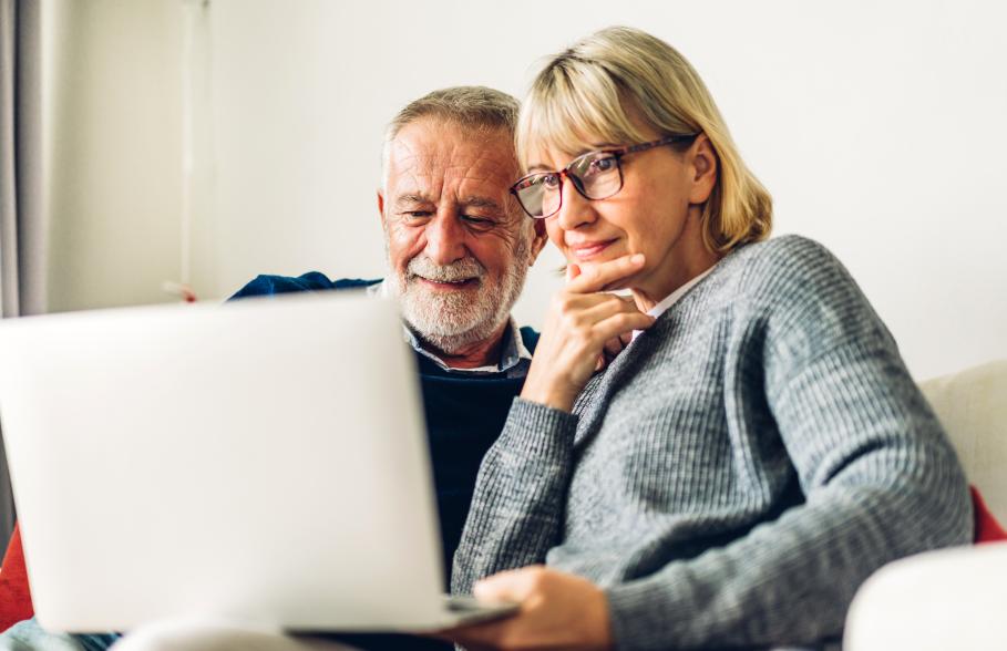 A couple use a laptop whilst sitting on the sofa