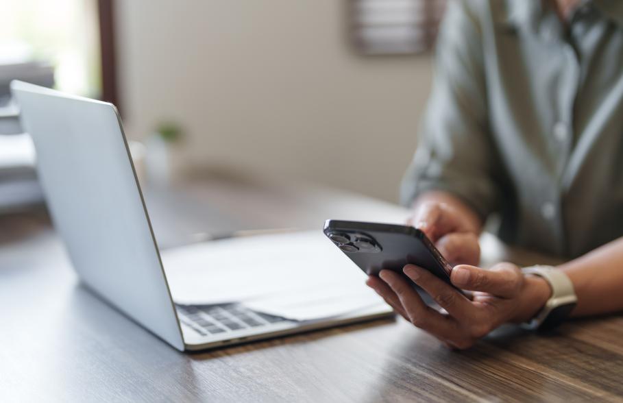 A person uses their mobile phone whilst sitting next to their laptop