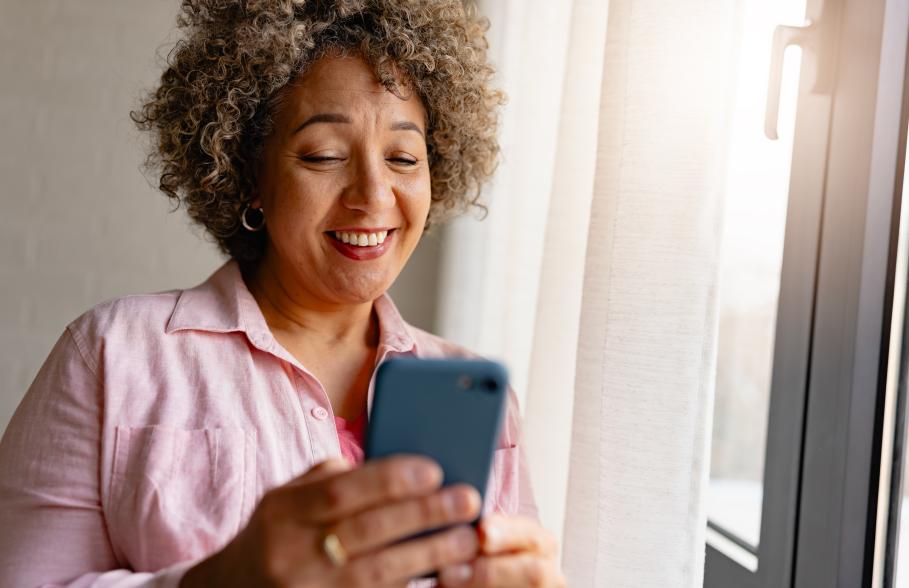 A woman checks her phone whilst standing beside a window