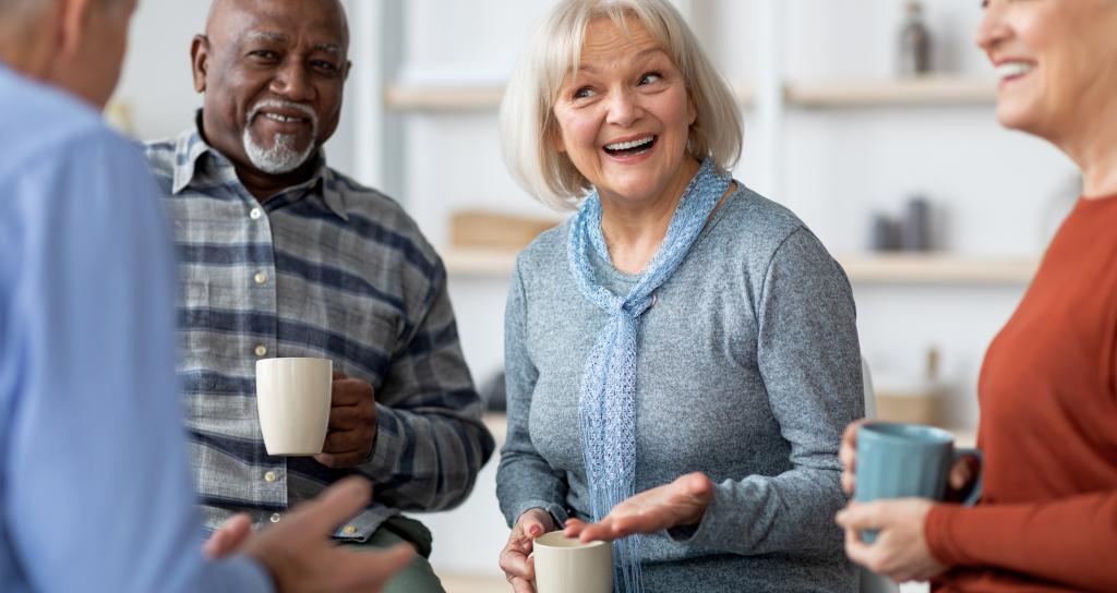 Four people in a group smiling whilst holding cups of coffee