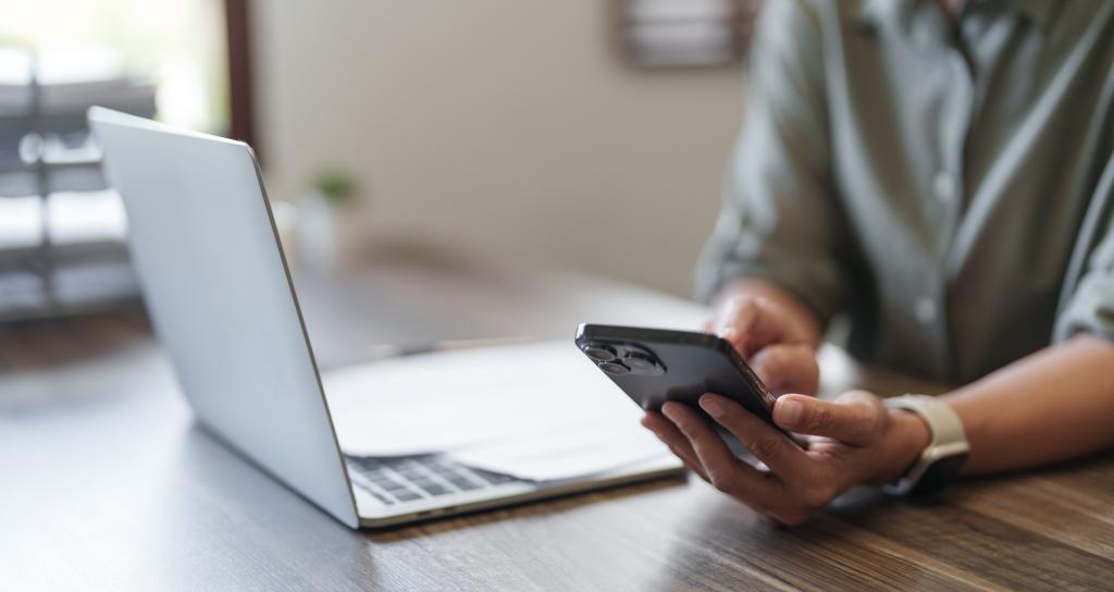 A person uses their mobile phone whilst sitting next to their laptop